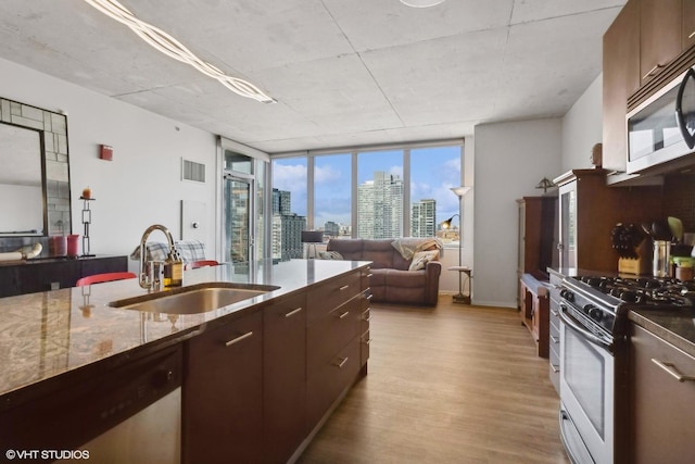 kitchen featuring dark brown cabinetry, sink, light wood-type flooring, stainless steel appliances, and light stone countertops