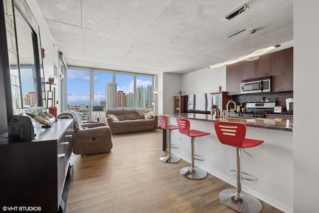 kitchen featuring appliances with stainless steel finishes, dark brown cabinets, a kitchen breakfast bar, tasteful backsplash, and light hardwood / wood-style floors