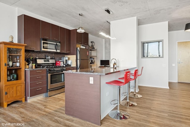 kitchen featuring appliances with stainless steel finishes, a breakfast bar, light wood-type flooring, and decorative light fixtures