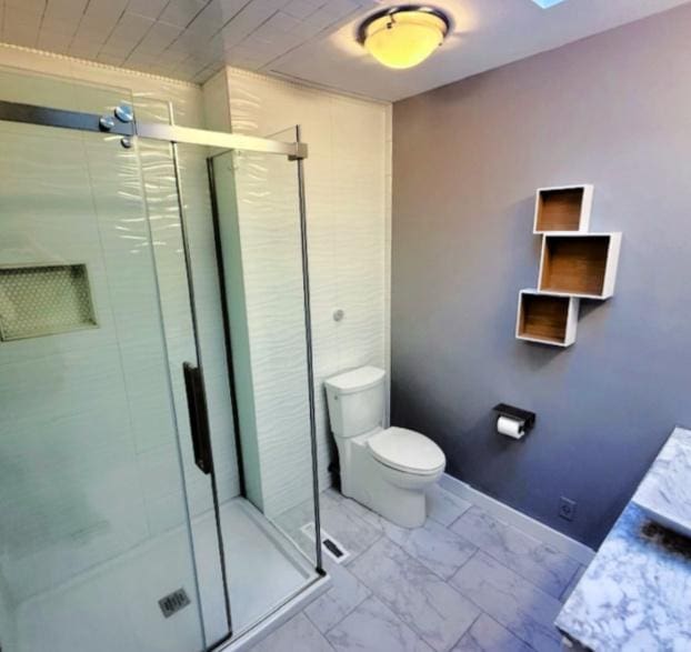 bathroom featuring a shower stall, toilet, baseboards, and marble finish floor