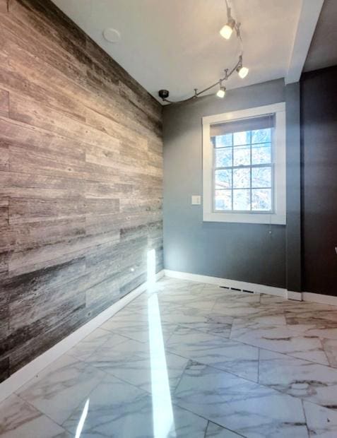 spare room featuring wooden walls, marble finish floor, rail lighting, and baseboards