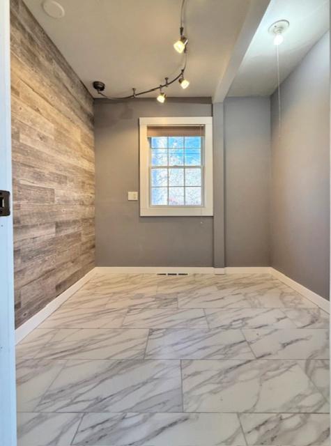 spare room with track lighting, marble finish floor, baseboards, and wood walls