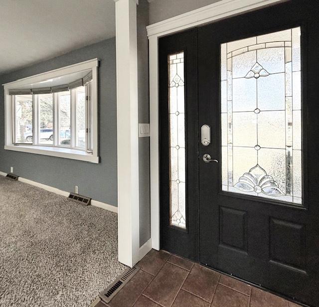 foyer entrance with baseboards, visible vents, and dark carpet