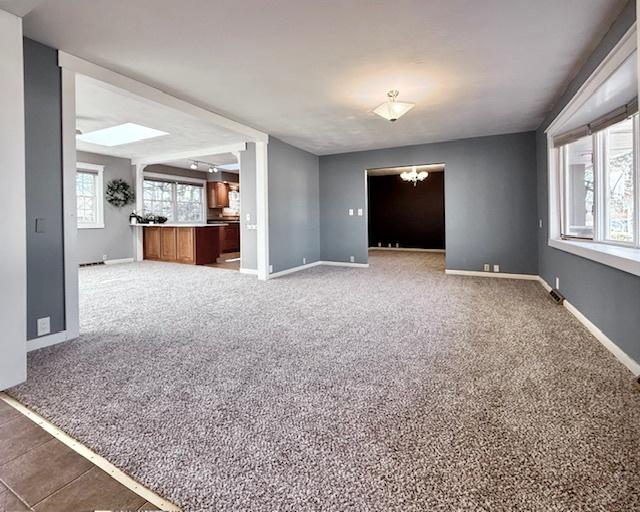 empty room featuring a notable chandelier, carpet flooring, and baseboards