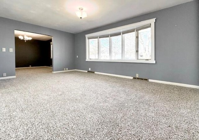 carpeted empty room featuring visible vents, baseboards, and a notable chandelier