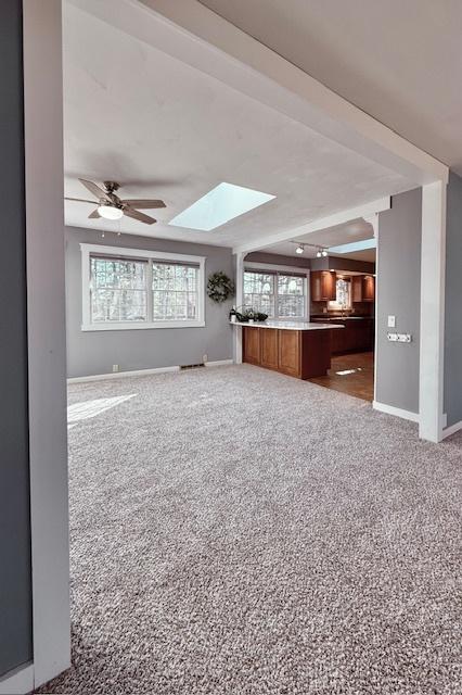 unfurnished living room featuring carpet flooring, a skylight, baseboards, and a ceiling fan