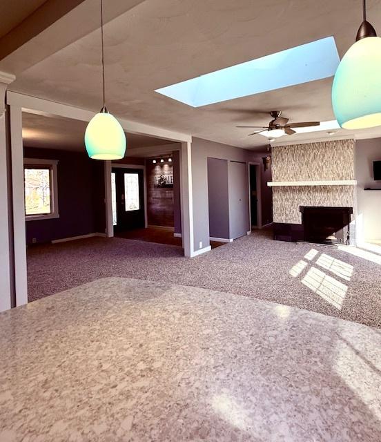 unfurnished living room with ceiling fan, a large fireplace, carpet floors, and a skylight