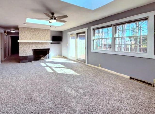 unfurnished living room featuring visible vents, a skylight, a ceiling fan, and carpet floors