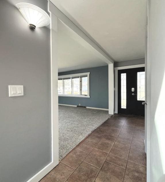 foyer entrance featuring baseboards and dark colored carpet