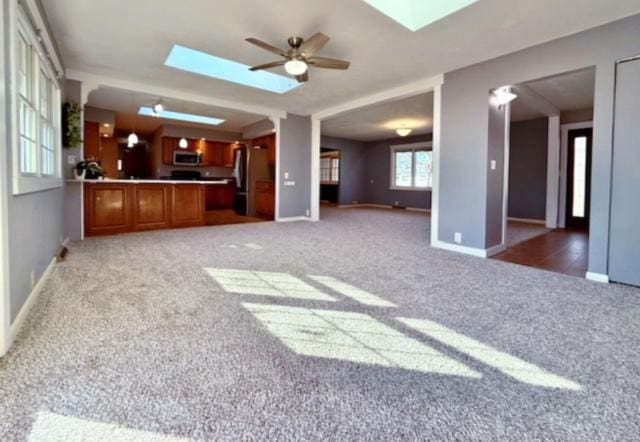 unfurnished living room featuring light colored carpet, a skylight, and baseboards