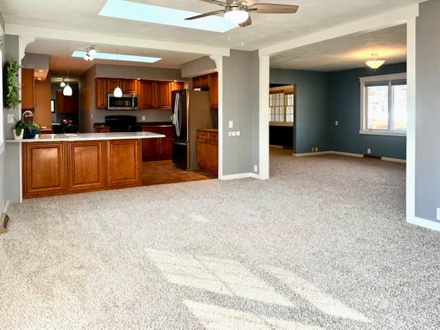 kitchen with carpet, open floor plan, brown cabinets, a peninsula, and stainless steel appliances