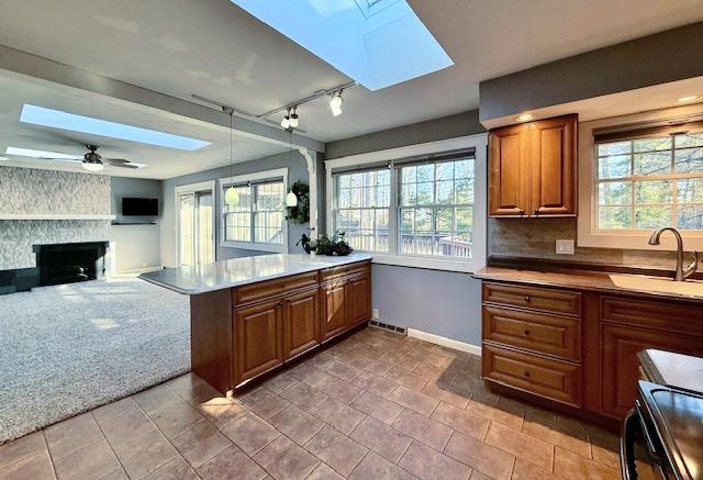 kitchen featuring carpet floors, brown cabinets, a skylight, plenty of natural light, and a sink