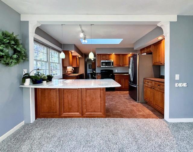 kitchen with stainless steel appliances, carpet floors, a peninsula, and brown cabinetry