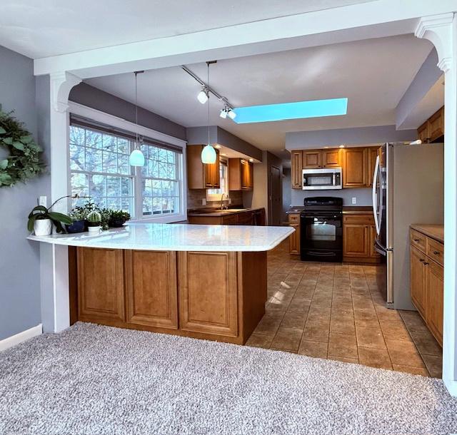 kitchen featuring brown cabinetry, a peninsula, a sink, stainless steel appliances, and light countertops