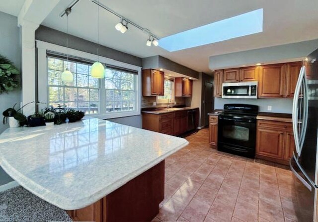 kitchen with brown cabinets, a peninsula, a skylight, stainless steel appliances, and a sink