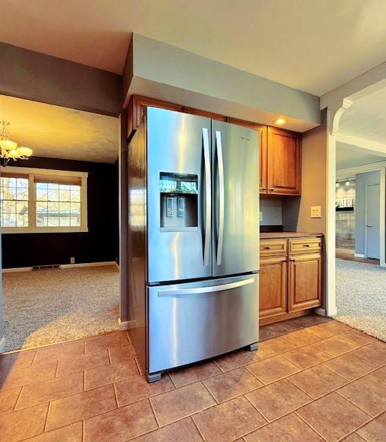 kitchen featuring brown cabinetry, light colored carpet, an inviting chandelier, and stainless steel fridge with ice dispenser