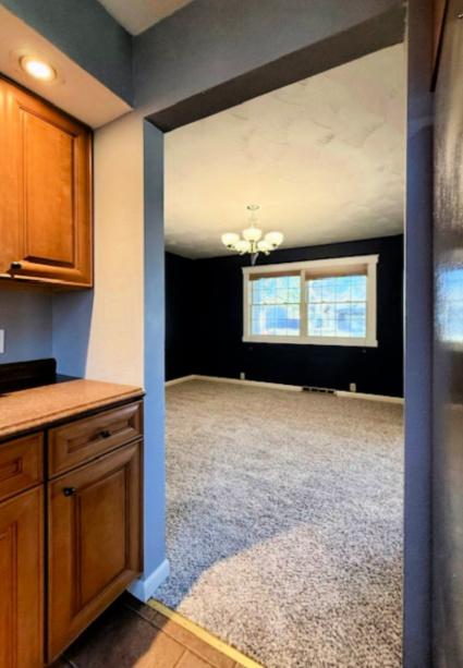 kitchen with brown cabinetry, a chandelier, baseboards, and carpet