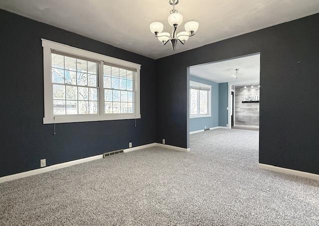 spare room with an inviting chandelier, carpet flooring, baseboards, and visible vents