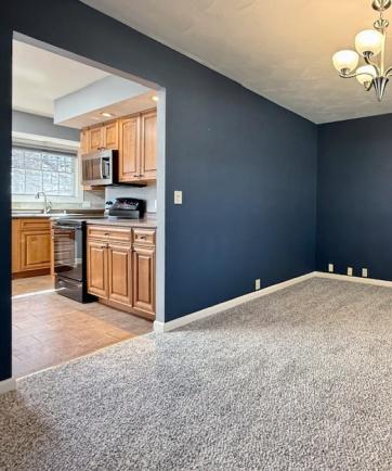 kitchen featuring stainless steel microwave, baseboards, light colored carpet, black electric range, and a notable chandelier