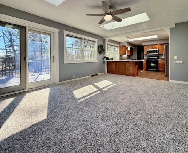 unfurnished living room featuring a skylight, light colored carpet, baseboards, and ceiling fan