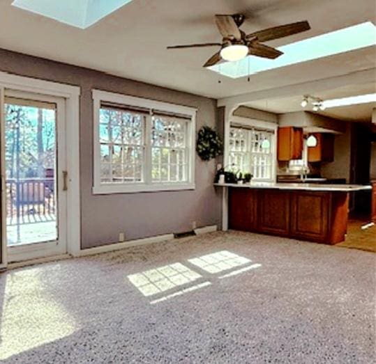 interior space with a ceiling fan, a peninsula, a skylight, light countertops, and brown cabinets