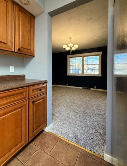 kitchen featuring dark countertops, brown cabinets, light colored carpet, and an inviting chandelier