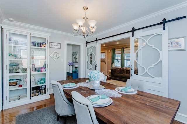 dining area with crown molding, a barn door, an inviting chandelier, and hardwood / wood-style floors