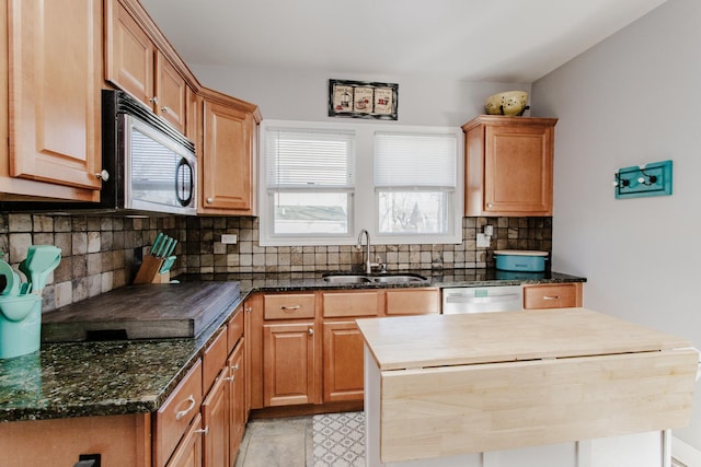 kitchen featuring sink, appliances with stainless steel finishes, dark stone countertops, backsplash, and a kitchen island