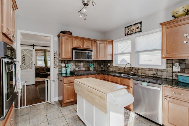 kitchen featuring appliances with stainless steel finishes, tasteful backsplash, sink, dark stone countertops, and a barn door