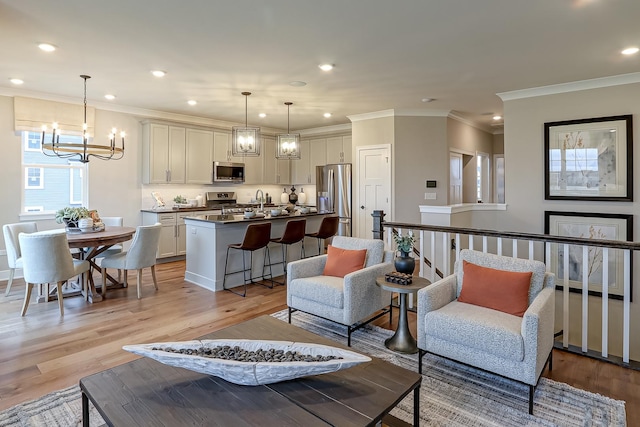 living room with crown molding, sink, light hardwood / wood-style flooring, and a notable chandelier