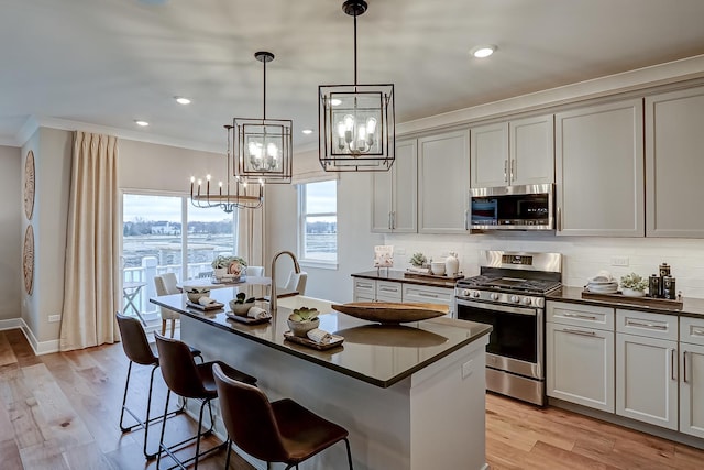 kitchen with tasteful backsplash, hanging light fixtures, stainless steel appliances, and a center island with sink