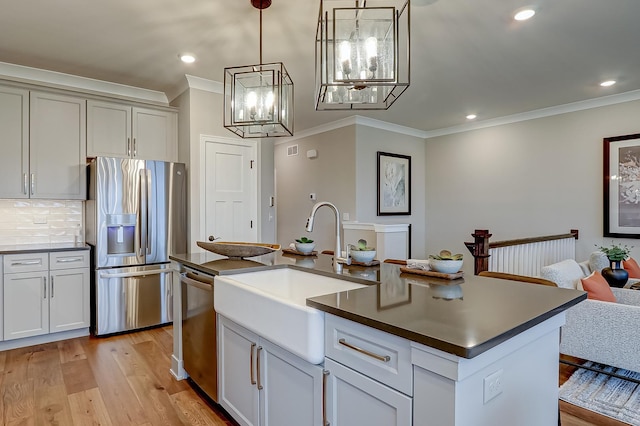 kitchen with ornamental molding, appliances with stainless steel finishes, sink, and a kitchen island with sink