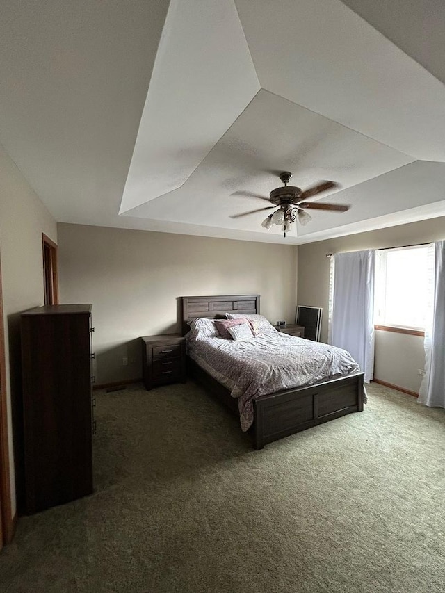 bedroom featuring a raised ceiling, ceiling fan, and dark colored carpet