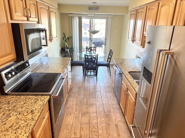 kitchen with hanging light fixtures, appliances with stainless steel finishes, a fireplace, and light hardwood / wood-style floors