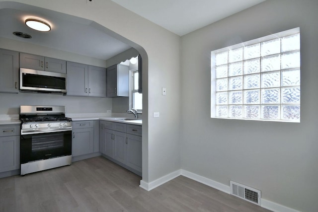 kitchen featuring light wood-type flooring, appliances with stainless steel finishes, sink, and gray cabinetry