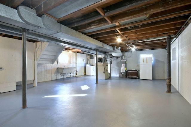 basement featuring sink, water heater, white refrigerator, heating unit, and washer / dryer