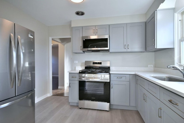 kitchen with stainless steel appliances, sink, gray cabinetry, and light hardwood / wood-style flooring