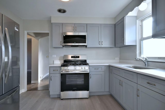 kitchen featuring stainless steel appliances, sink, gray cabinetry, and light hardwood / wood-style floors