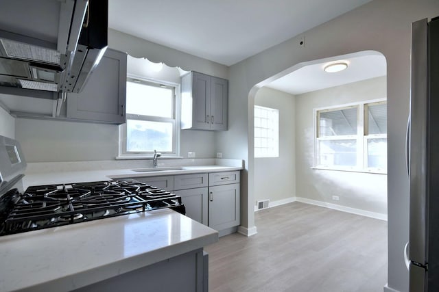 kitchen featuring sink, gray cabinets, stainless steel fridge, stove, and light wood-type flooring