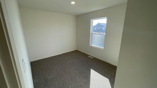 empty room featuring visible vents, baseboards, and dark colored carpet