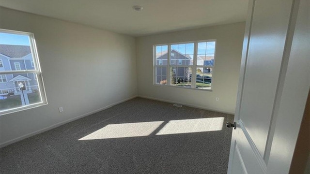 spare room featuring dark colored carpet, baseboards, and plenty of natural light