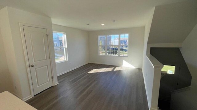 unfurnished living room with plenty of natural light, baseboards, and dark wood-style flooring