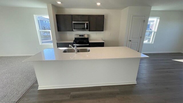 kitchen featuring baseboards, light countertops, appliances with stainless steel finishes, dark wood-style floors, and a sink