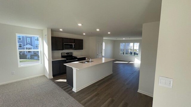 kitchen featuring an island with sink, a sink, open floor plan, stainless steel appliances, and light countertops