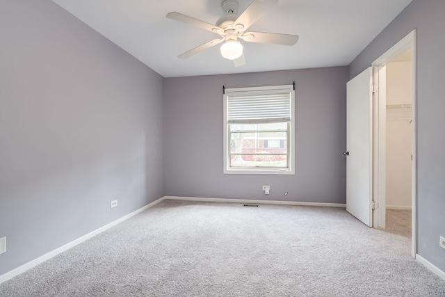 unfurnished bedroom featuring baseboards, carpet flooring, a spacious closet, and ceiling fan
