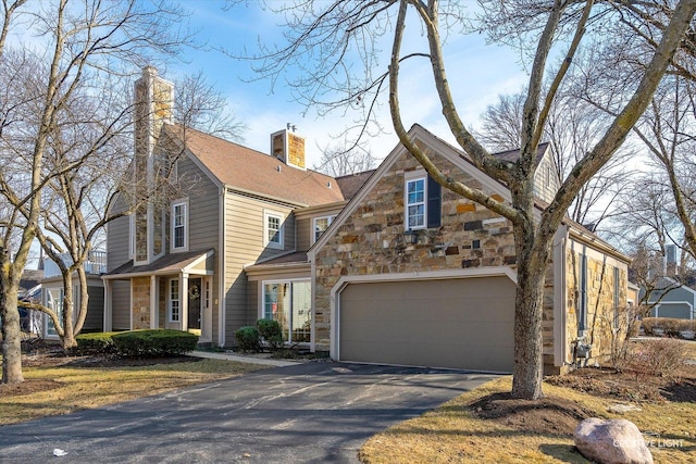 view of front of house featuring aphalt driveway, stone siding, a chimney, and a garage