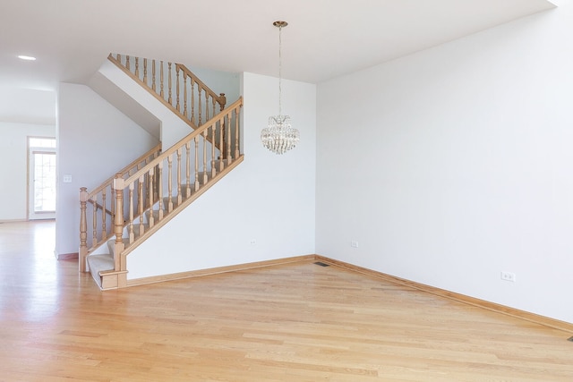 empty room featuring a notable chandelier, visible vents, wood finished floors, baseboards, and stairs