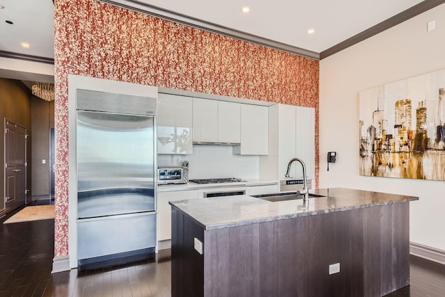 kitchen featuring sink, white cabinets, ornamental molding, stainless steel appliances, and a center island with sink