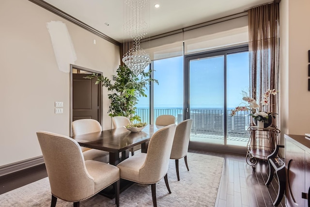 dining area with a notable chandelier, wood-type flooring, ornamental molding, and a water view