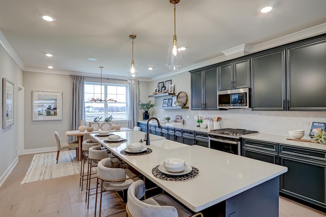 kitchen with a breakfast bar, stainless steel appliances, light hardwood / wood-style floors, and a center island with sink